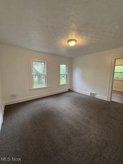 Empty room with dark colored carpet and a textured ceiling