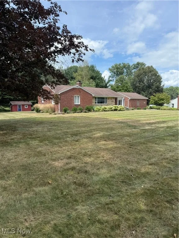 Single story home featuring a chimney, a front yard, and an outbuilding