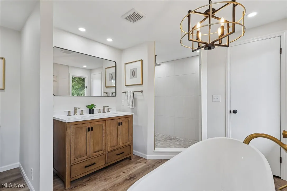 Full bathroom with a soaking tub, double vanity, a walk in shower, light wood finished floors, and recessed lighting