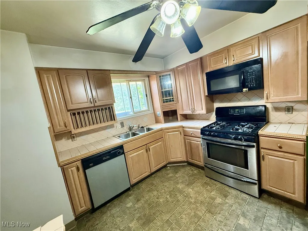 Kitchen with tile countertops, stainless steel appliances, decorative backsplash, and stone finish floors