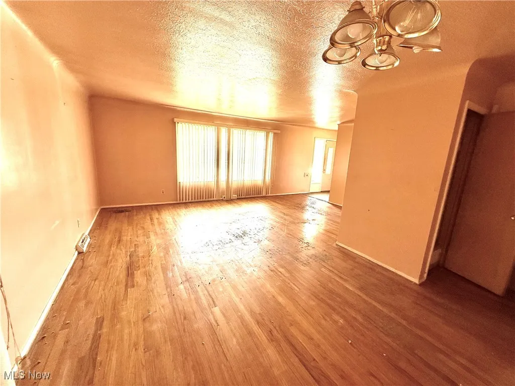 Empty room featuring wood finished floors, a textured ceiling, and a chandelier
