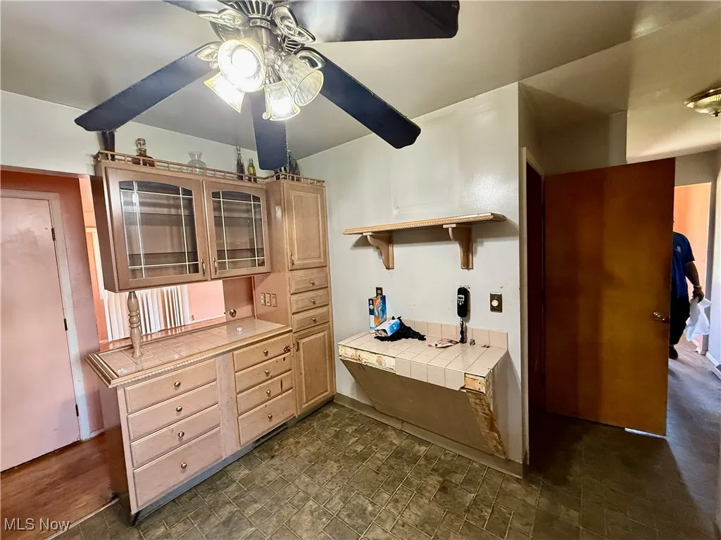 Kitchen with glass insert cabinets, tile countertops, open shelves, and light brown cabinetry