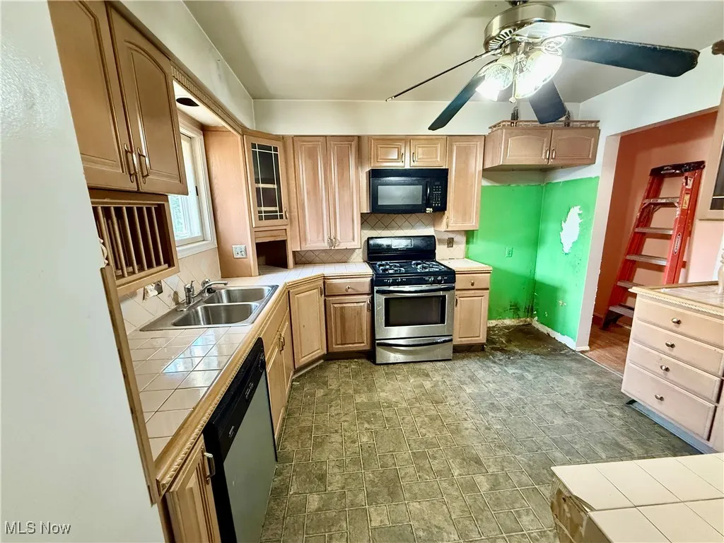 Kitchen featuring stainless steel appliances, tile countertops, decorative backsplash, glass insert cabinets, and a ceiling fan