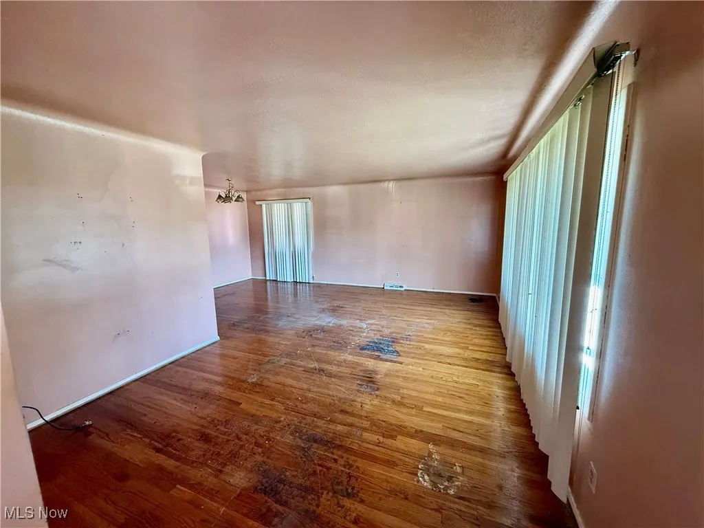 Empty room with dark wood finished floors and a chandelier