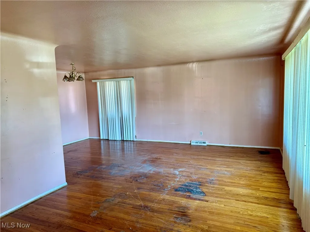 Empty room featuring a chandelier, hardwood / wood-style flooring, and a textured ceiling