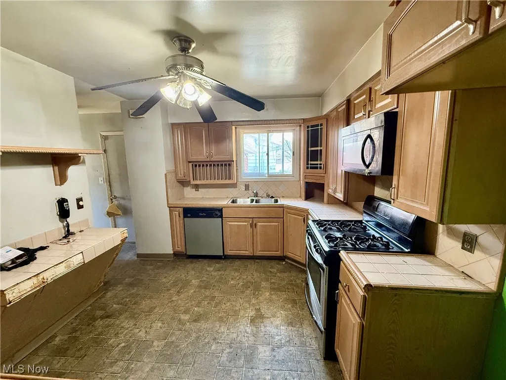 Kitchen featuring gas stove, tasteful backsplash, tile counters, black microwave, and stone finish floors