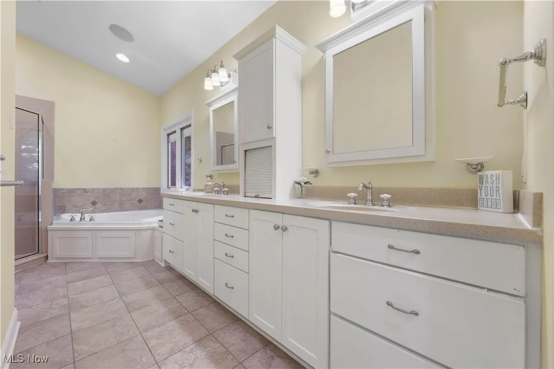 Primary bathroom featuring double vanity, a jacuzzi tub, a separate shower, tile flooring, and lofted ceiling