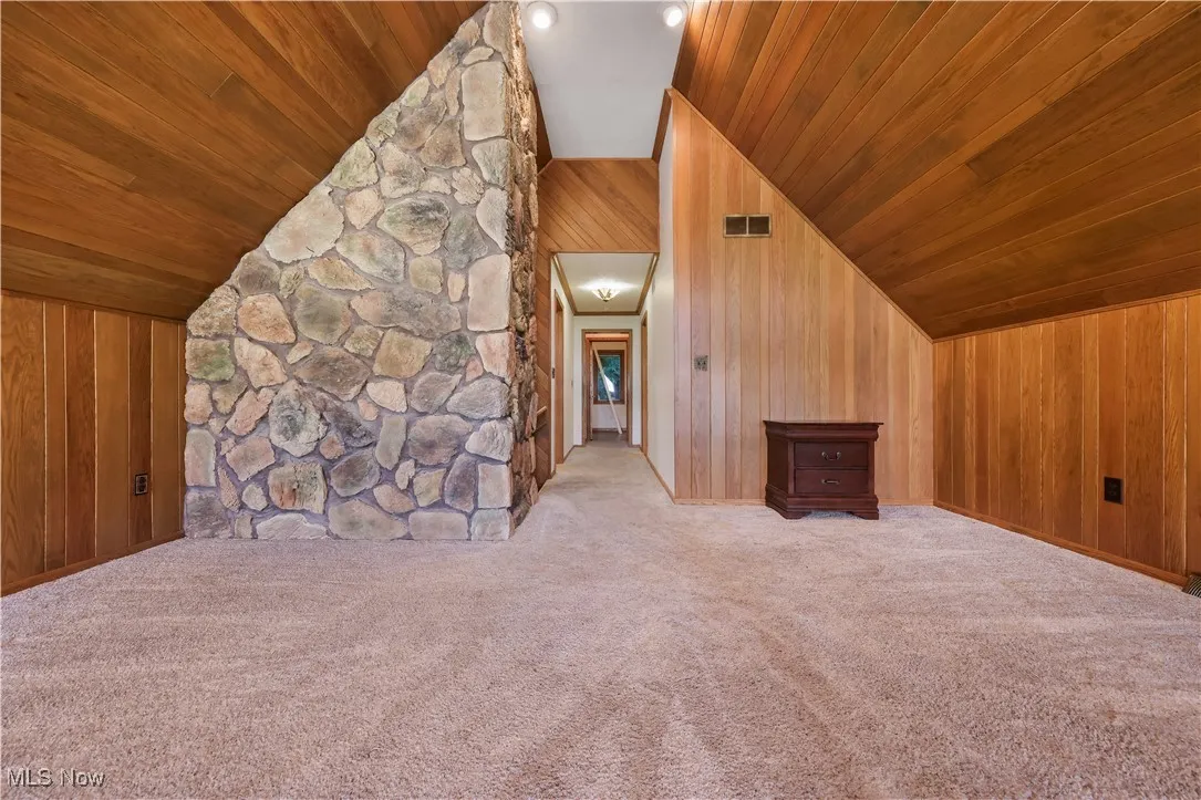 Loft featuring wooden and stone walls, carpet flooring, and A-frame, vaulted, planked ceiling
