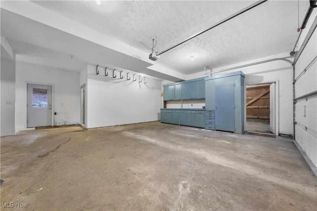 View of 2 car garage with workbench area, 2 large storage closets, backyard access and stairs that lead to the basement.