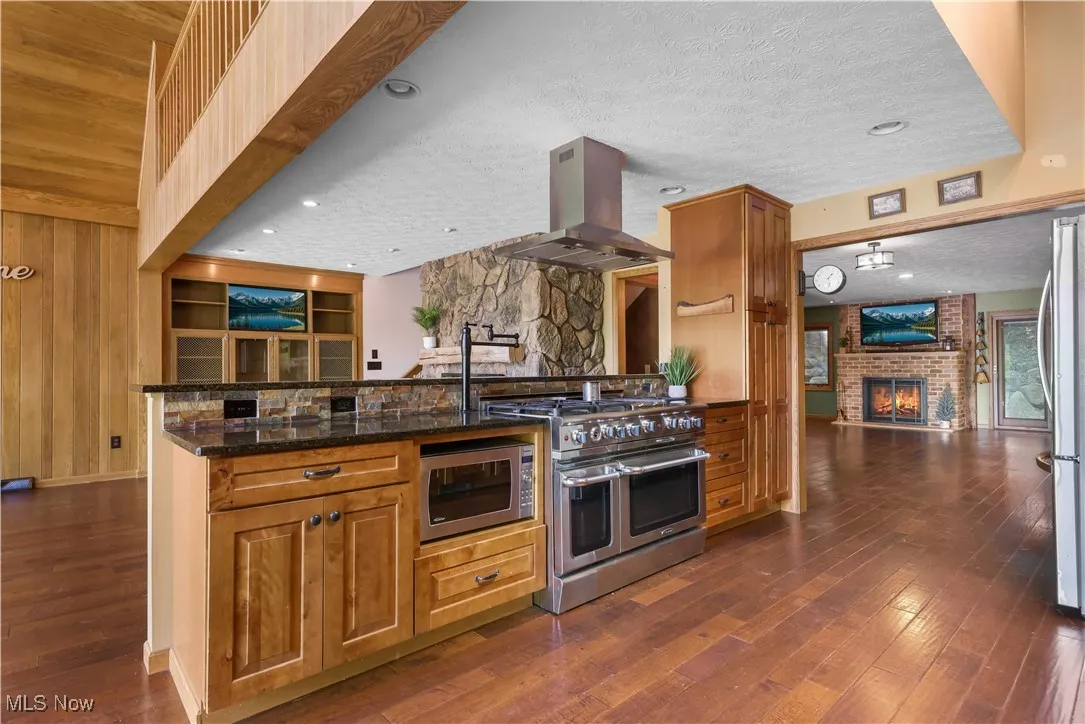 Kitchen with rustic cabinetry, island range hood, 2 dishwashers, gas stove, granite countertops, stone backsplash, stainless high-end appliances including pot filler and vaulted ceilings