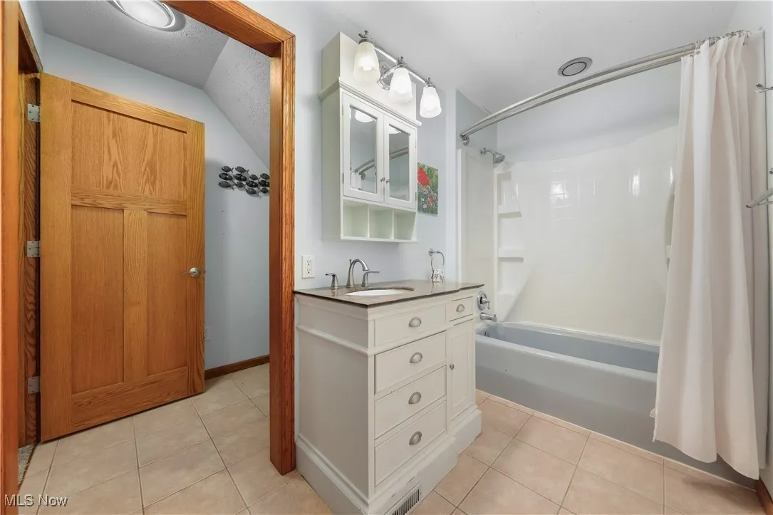 Full bathroom featuring shower / bath combo with ceramic tile floors, vanity and separate toilet area.