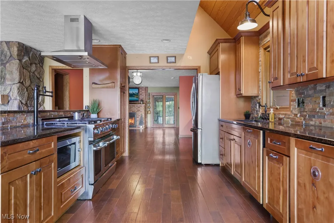 Kitchen with rustic cabinetry, island range hood, gas stove 2 dishwashers, granite countertops, stone backsplash, stainless, high-end appliances including pot filler and vaulted ceilings