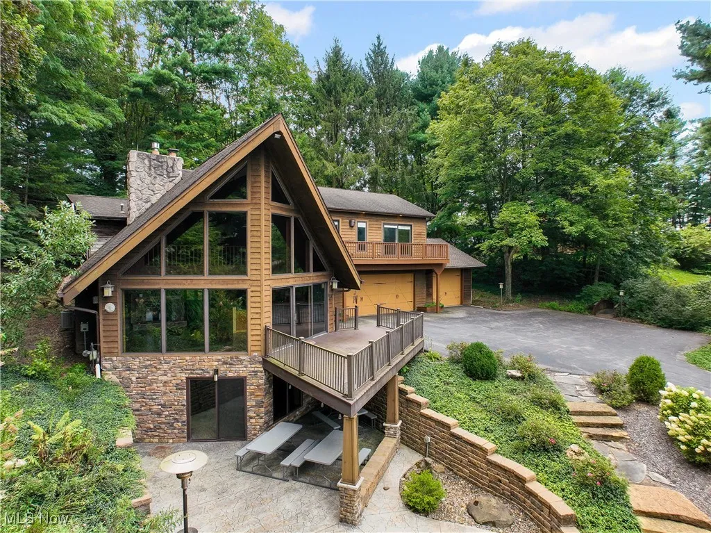 Front view of property with a stone chimney, patio, wood siding, deck, and a stonestairway leading to the driveway