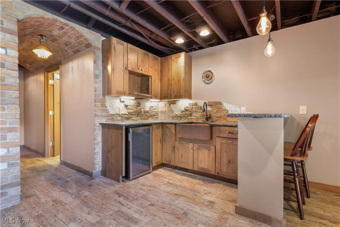 LL bar/kitchenette area featuring pendant lighting, stone counters, brick backsplash, wine cooler, and arched brick hallway that leads to a full bathroom.