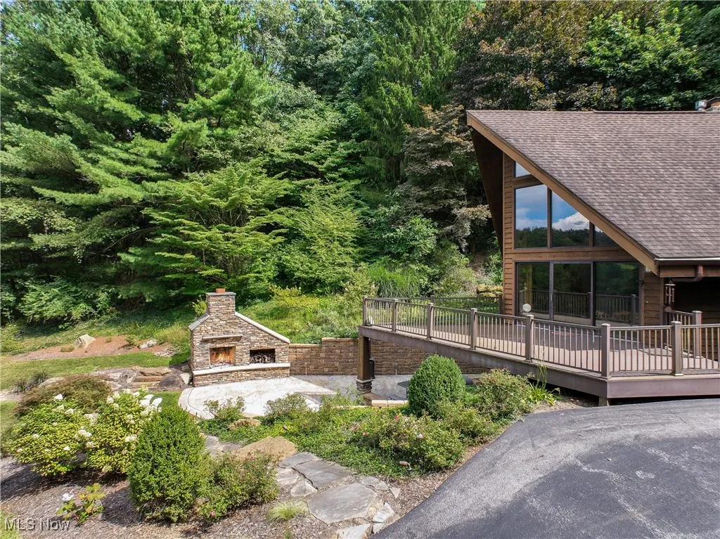 View of side of home featuring an outdoor stone fireplace, patio and a wooden deck off the kitchen/dining room