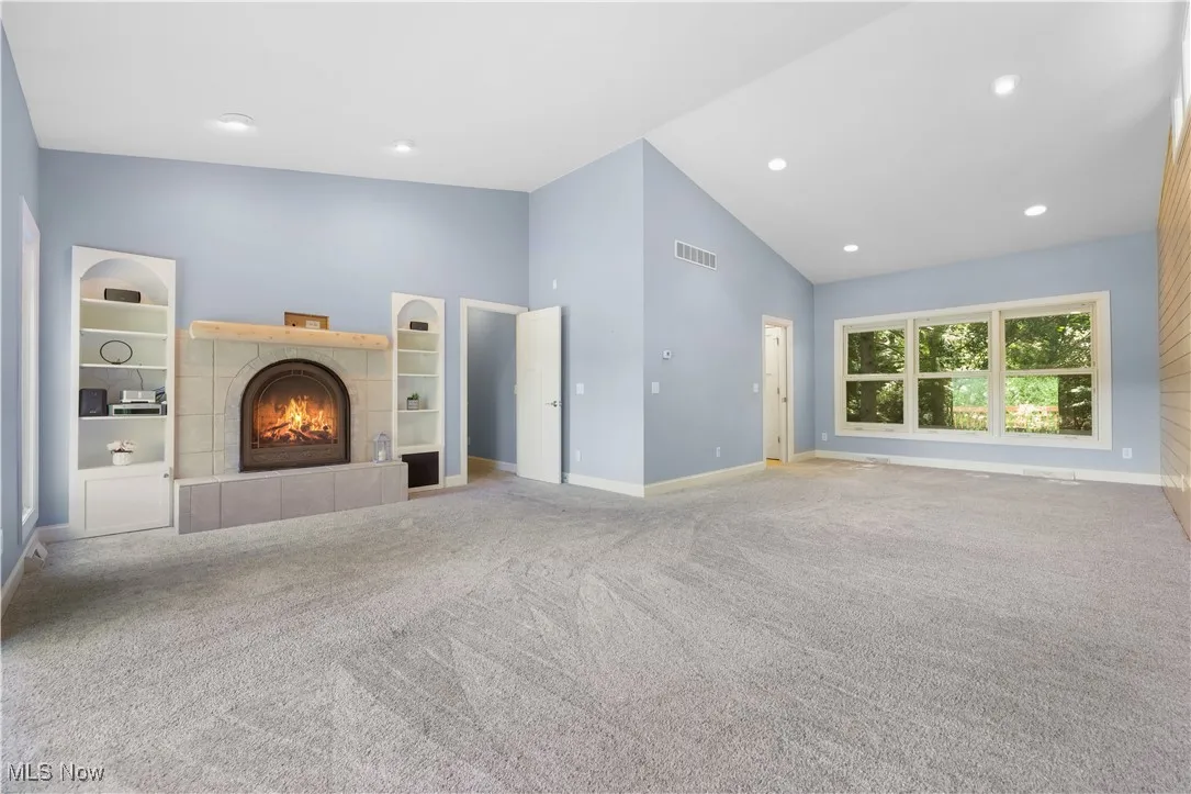 Primary bedroom with a tile fireplace, built-in shelving, vaulted ceilings and access to the primary bathroom.