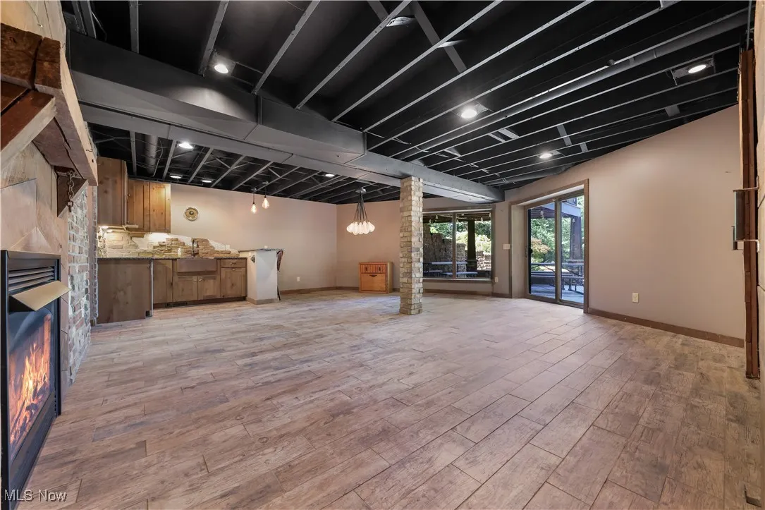LL walk-out to patio featuring a stone outdoor fireplace and indoor kitchenette w wine fridge, warm fireplace and wood-style floors