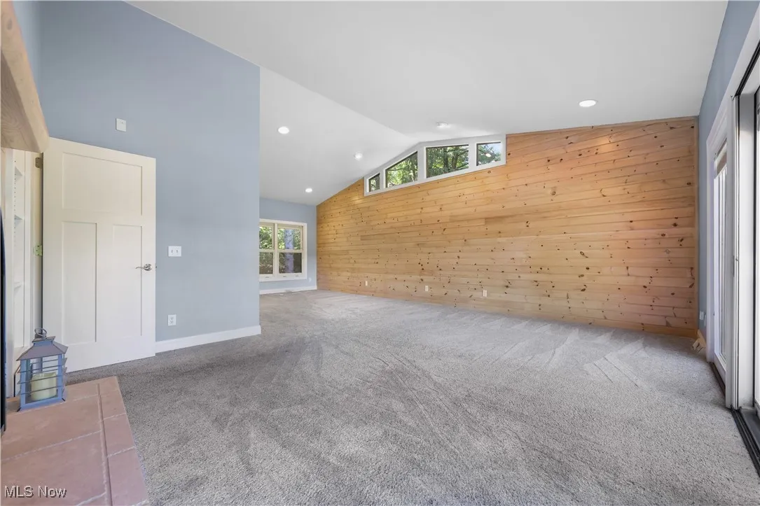 Primary bedroom with knotted pine accent wall, vaulted ceiling, recessed lighting and fireplace.