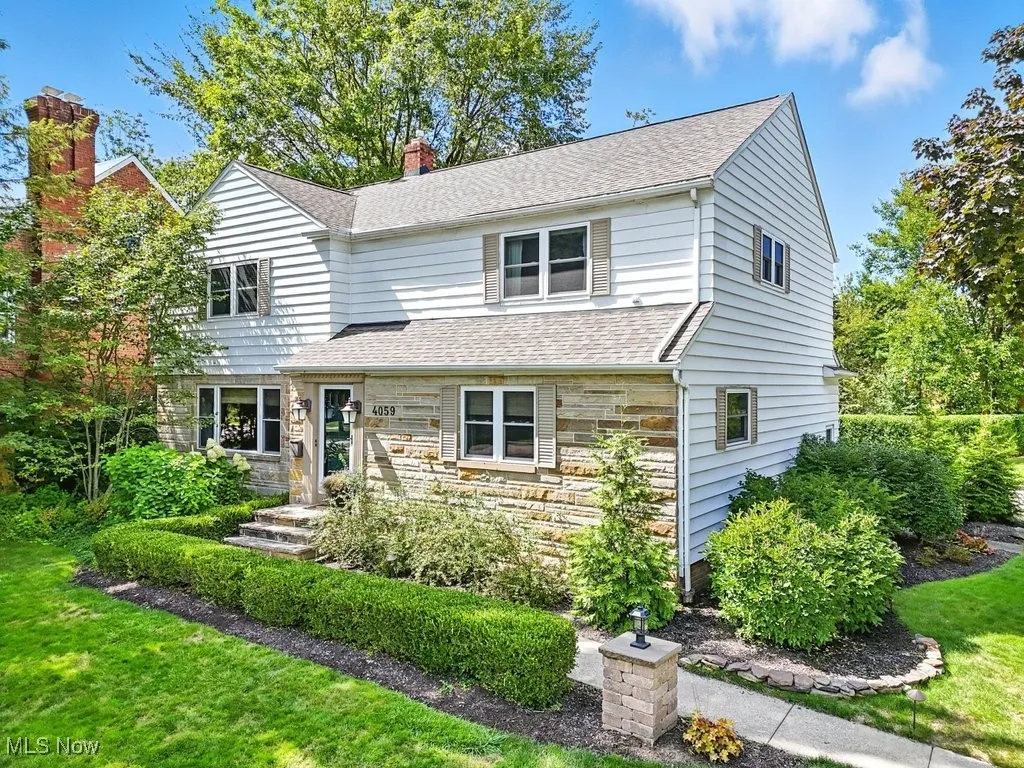 Traditional home with stone siding, a chimney, roof with shingles, and a front lawn