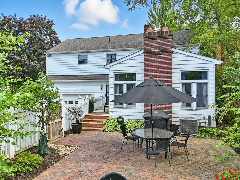 Rear view of property featuring a patio, a chimney, outdoor dining area, an attached garage, and roof with shingles