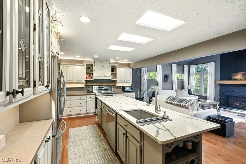Kitchen with open shelves, dark wood-style floors, an island with sink, light stone countertops, and appliances with stainless steel finishes