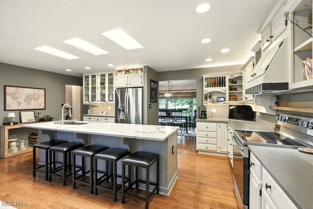 Kitchen with appliances with stainless steel finishes, a center island with sink, open shelves, white cabinetry, and glass insert cabinets