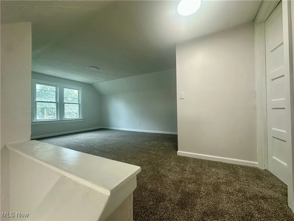 Bonus room with dark colored carpet, vaulted ceiling, and a textured ceiling
