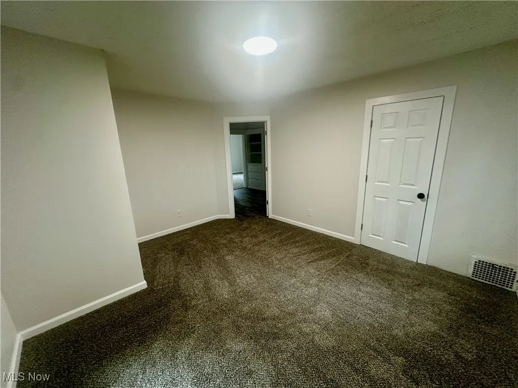 Unfurnished bedroom featuring dark colored carpet and baseboards