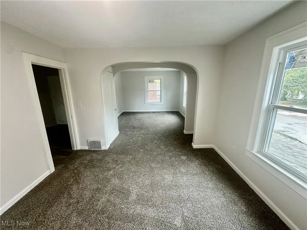 Empty room with dark carpet, arched walkways, and a textured ceiling