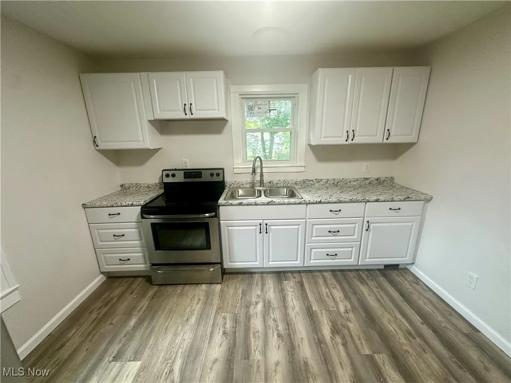 Kitchen featuring electric stove, white cabinetry, light wood-type flooring, and light stone countertops