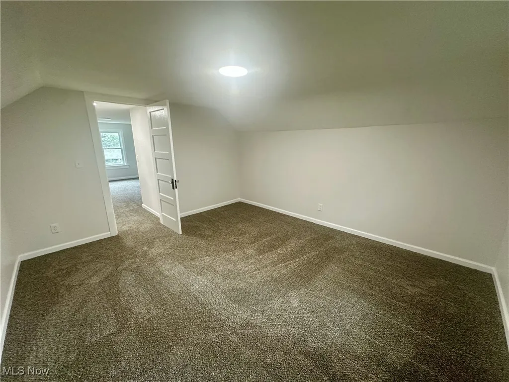 Additional living space with vaulted ceiling and dark carpet