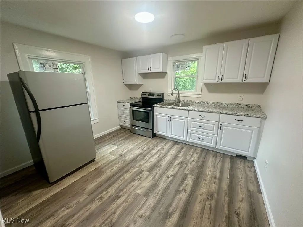 Kitchen featuring appliances with stainless steel finishes, white cabinets, light wood-type flooring, and light stone counters