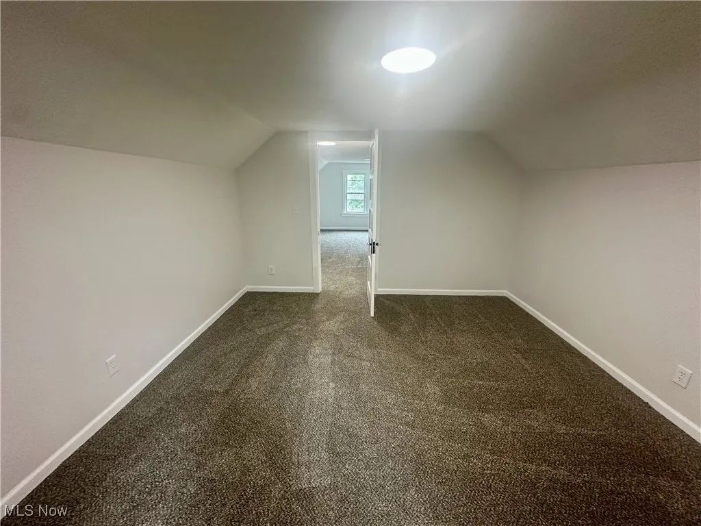 Bonus room with lofted ceiling and dark colored carpet