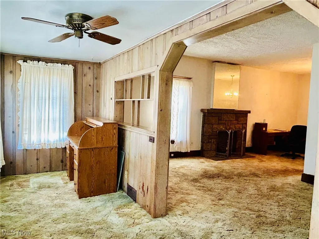 Foyer with wood walls, light colored carpet, arched walkways, ceiling fan, and stairway