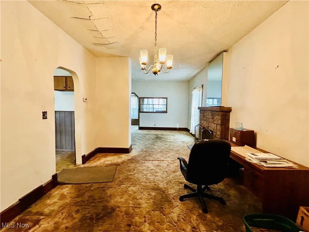 Unfurnished living room with carpet, wood walls, a stone fireplace, a ceiling fan, and a textured ceiling