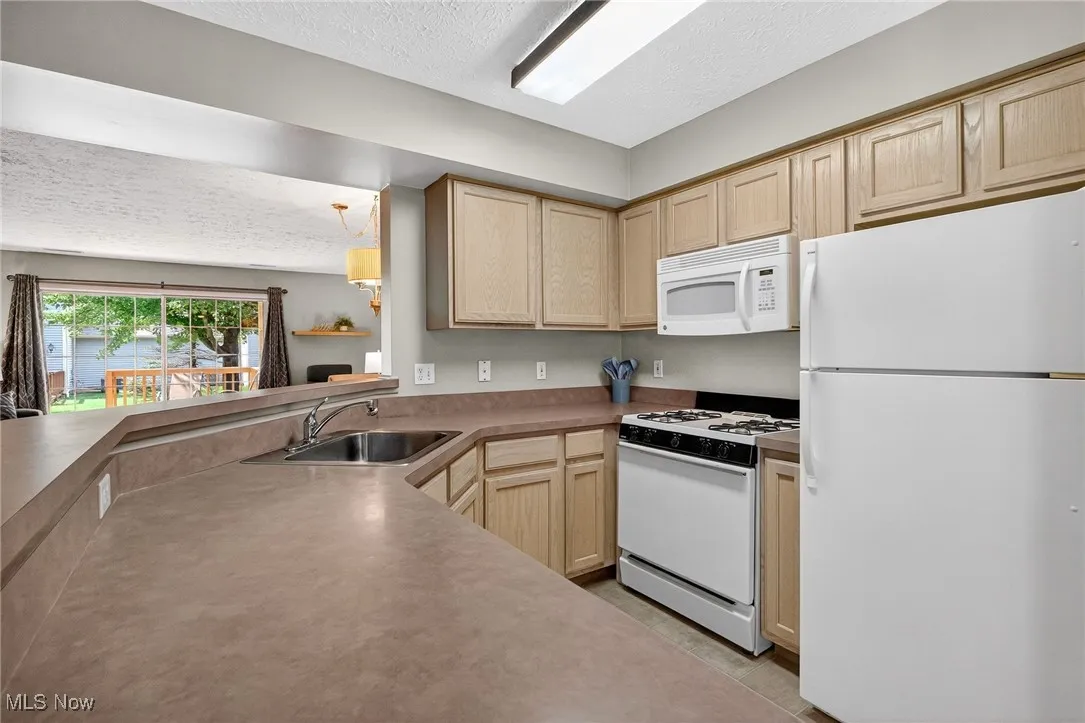 Kitchen featuring white appliances, a textured ceiling, light brown cabinetry, light tile patterned floors, and light countertops