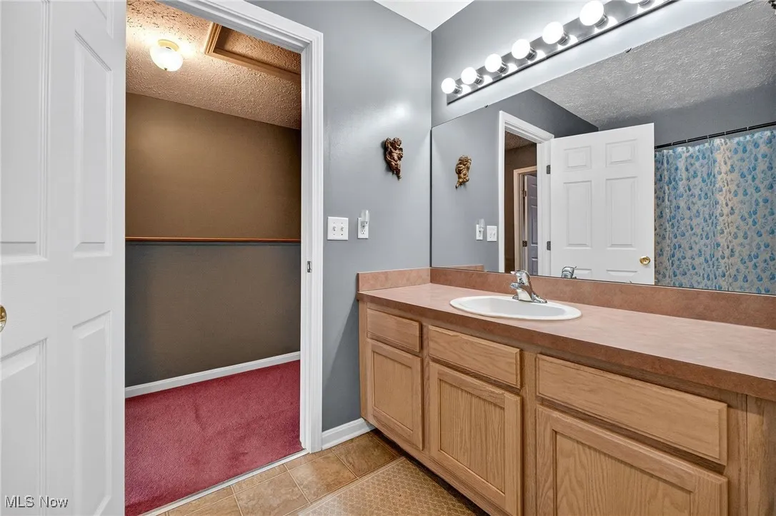 Bathroom with a textured ceiling, vanity, light tile patterned floors, and a shower with shower curtain