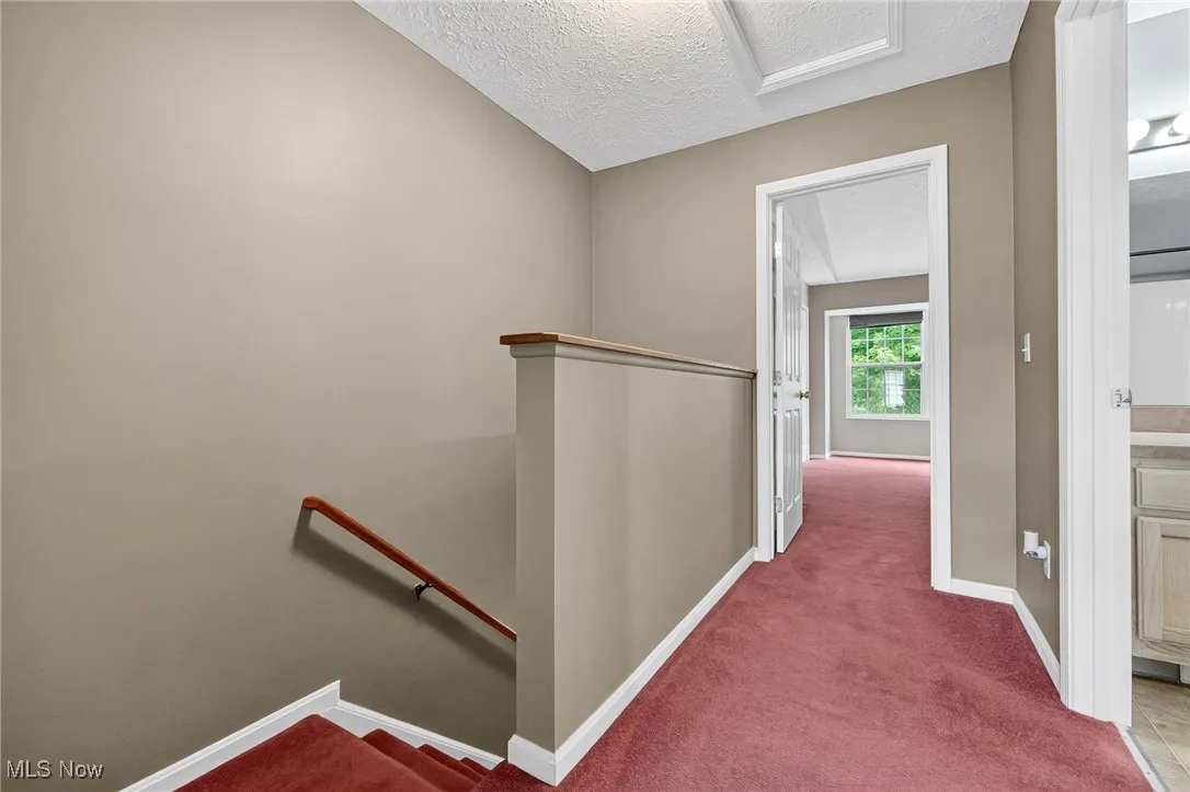 Corridor featuring an upstairs landing, a textured ceiling, and carpet