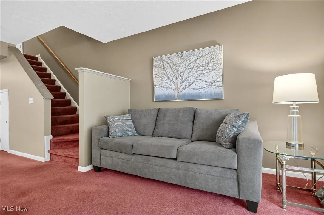 Carpeted living area with stairway and baseboards