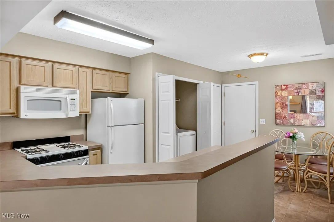 Kitchen with white appliances, a textured ceiling, light brown cabinetry, light countertops, and light tile patterned floors