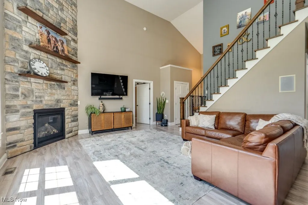 Living area with a fireplace, stairway, wood finished floors, and high vaulted ceiling