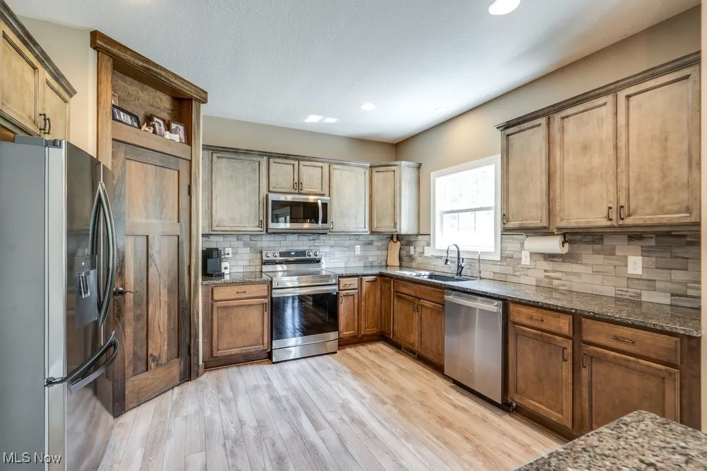 Kitchen featuring appliances with stainless steel finishes, dark stone counters, light wood-type flooring, decorative backsplash, and recessed lighting