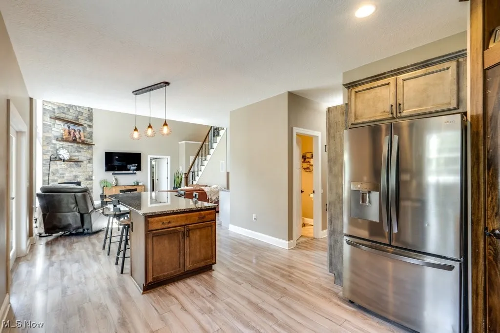 Kitchen featuring stainless steel fridge with ice dispenser, a breakfast bar area, dark stone countertops, pendant lighting, and open floor plan