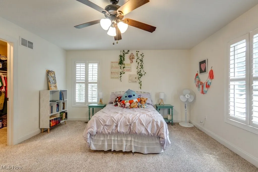 Bedroom featuring light colored carpet, a walk in closet, and a ceiling fan