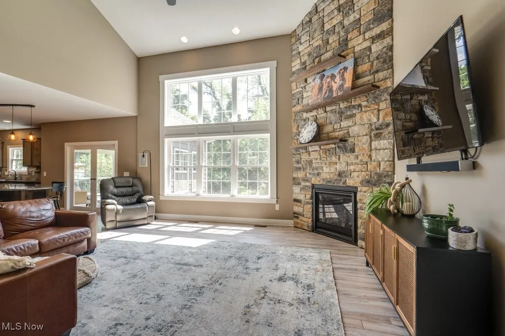 Living room with a towering ceiling, a stone fireplace, light wood finished floors, and recessed lighting