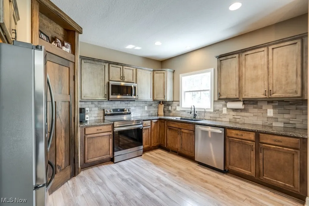 Kitchen with appliances with stainless steel finishes, dark stone countertops, light wood-style floors, tasteful backsplash, and recessed lighting