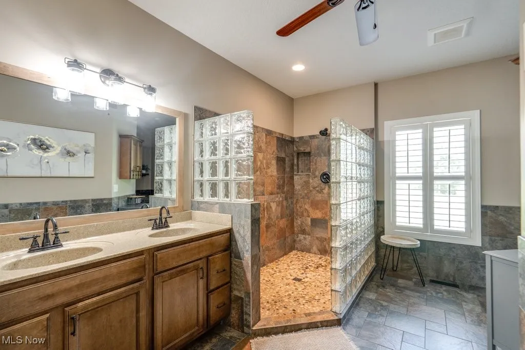 Bathroom featuring tile walls, a walk in shower, double vanity, stone tile flooring, and a wainscoted wall