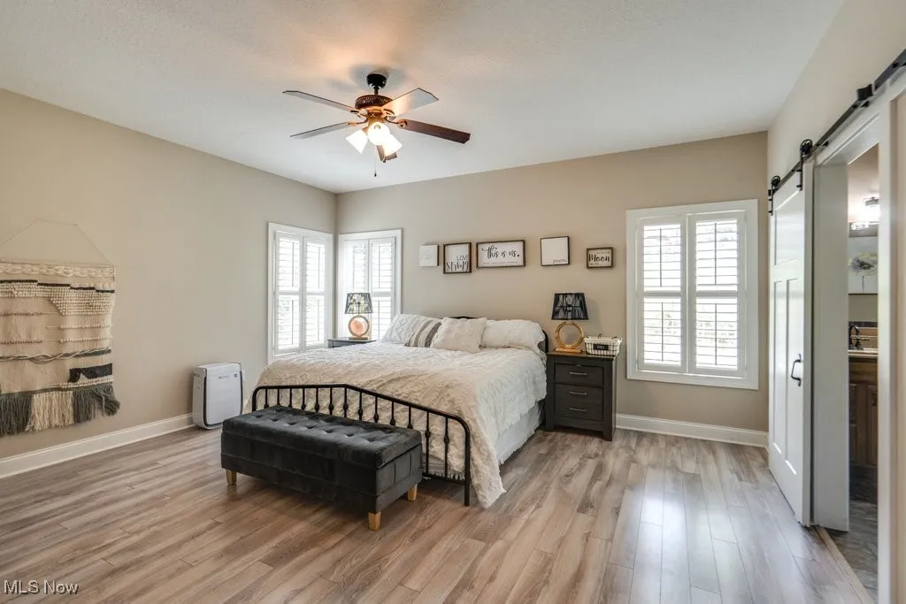Bedroom with a barn door, light wood-style flooring, and multiple windows