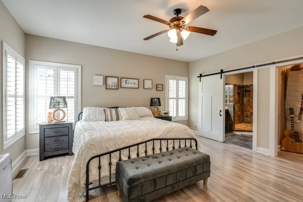 Bedroom featuring a barn door, light wood finished floors, a ceiling fan, and ensuite bath