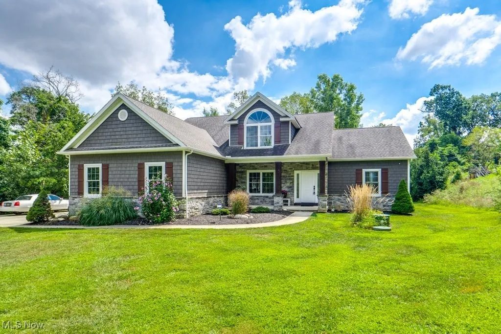 View of front of property featuring a porch, stone siding, a front yard, and a shingled roof